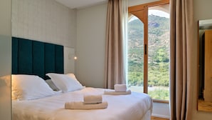 A hotel room with a large bed, a view of a mountainous landscape, and a wooden floor.
