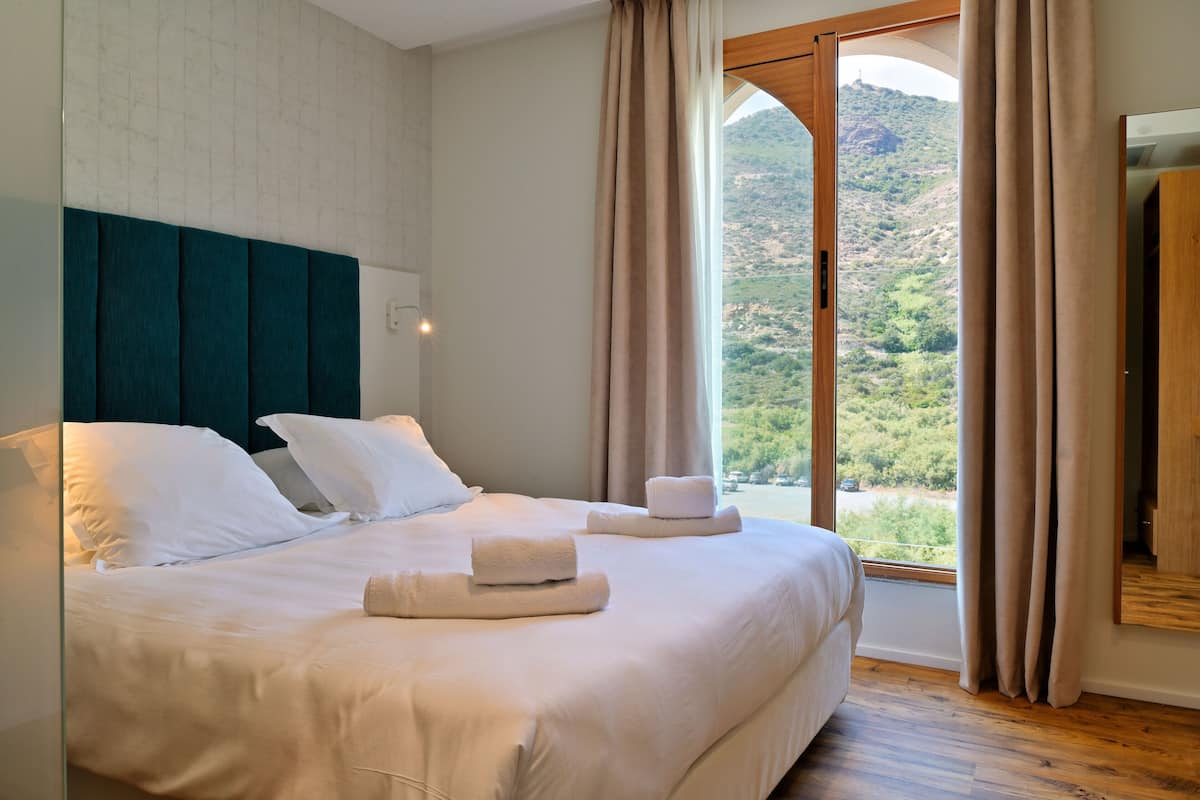 Una habitación de hotel con una cama grande, vistas a un paisaje montañoso y suelo de madera.