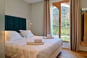 Una habitación de hotel con una cama grande, vistas a un paisaje montañoso y suelo de madera.