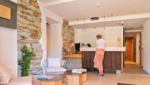 A modern reception area with a stone wall, a reception desk, and a seating area with a white chair and a round table.