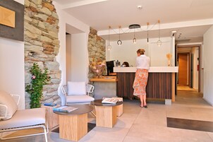 Un área de recepción moderna con una pared de piedra, una mesa de recepción y un espacio de espera con una silla blanca y una mesa redonda.