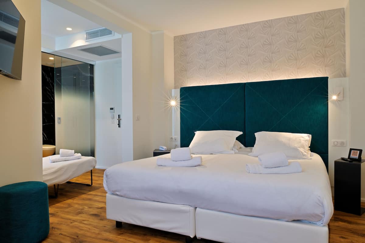 Una habitación de hotel moderna con una cama grande, una pared de acento color aguamarina y un separador de vidrio.