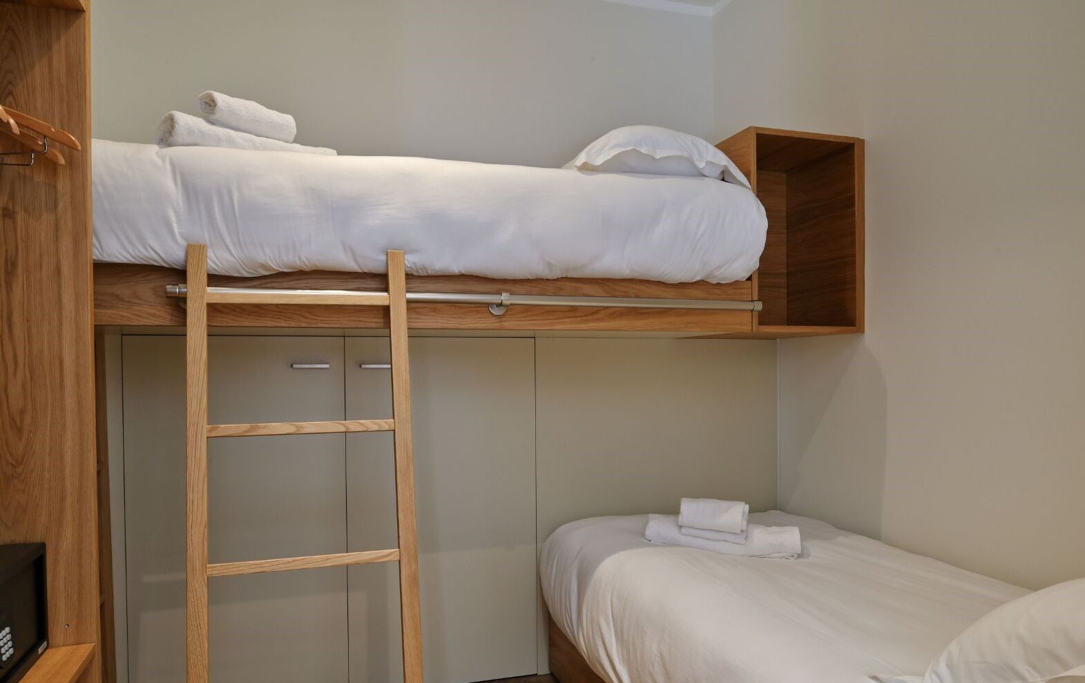 A bunk bed with a wooden ladder, a small shelf, and a single bed below.