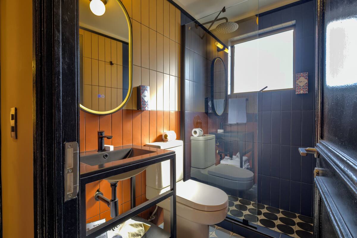 Un baño moderno con suelo a cuadros blancos y negros, inodoro blanco, lavamanos con espejo y zona de ducha.