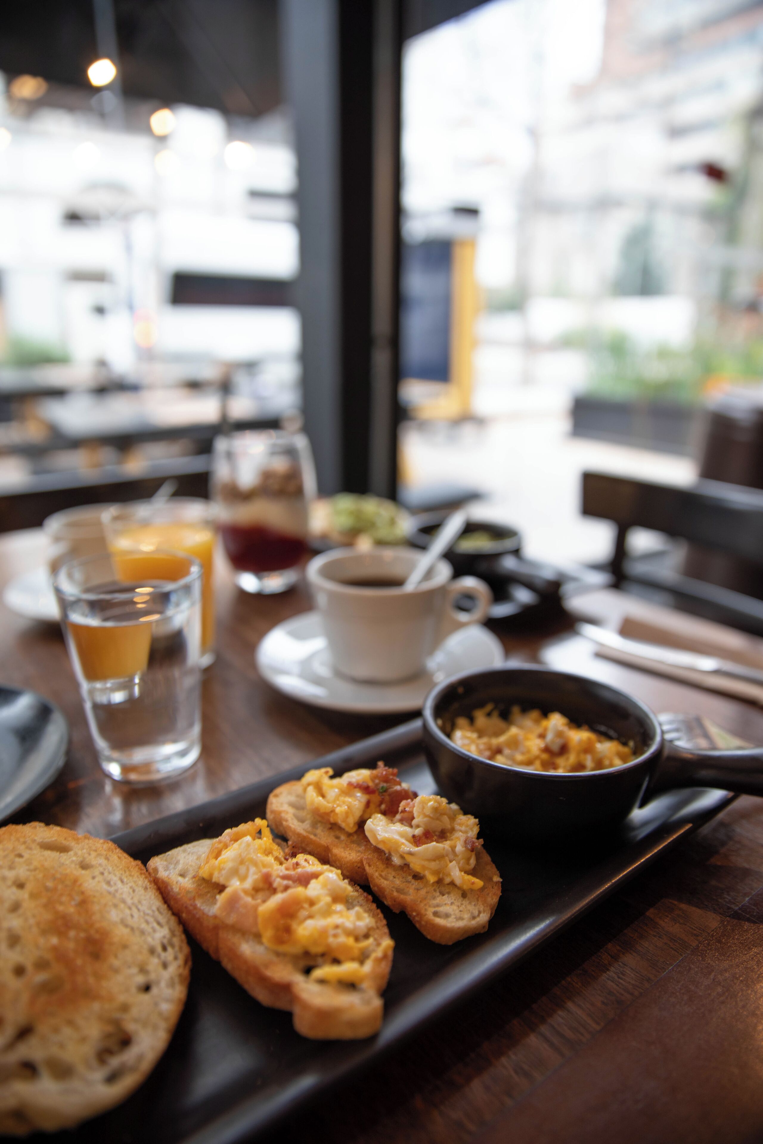 A breakfast tray with toast, scrambled eggs, and a bowl of soup on a wooden table in a restaurant.