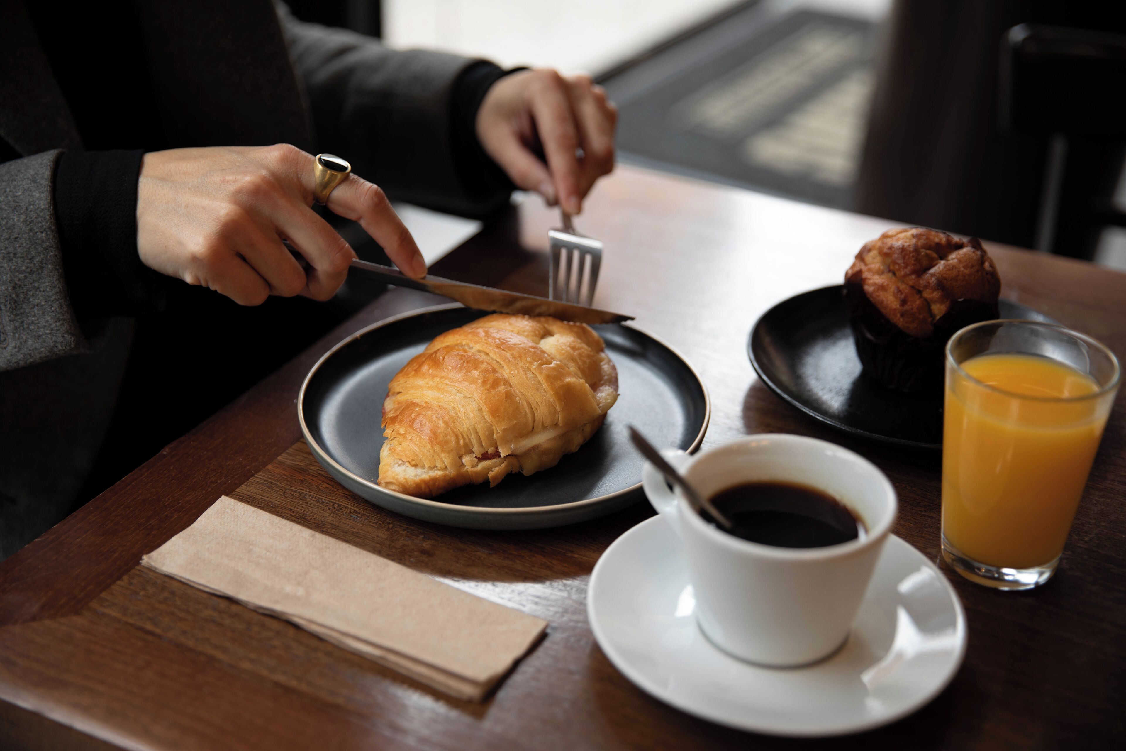 A breakfast setting with a croissant, muffin, cup of coffee, and glass of orange juice on a table.