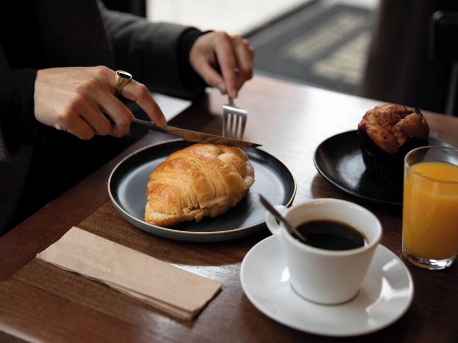 A breakfast setting with a croissant, muffin, cup of coffee, and glass of orange juice on a table.