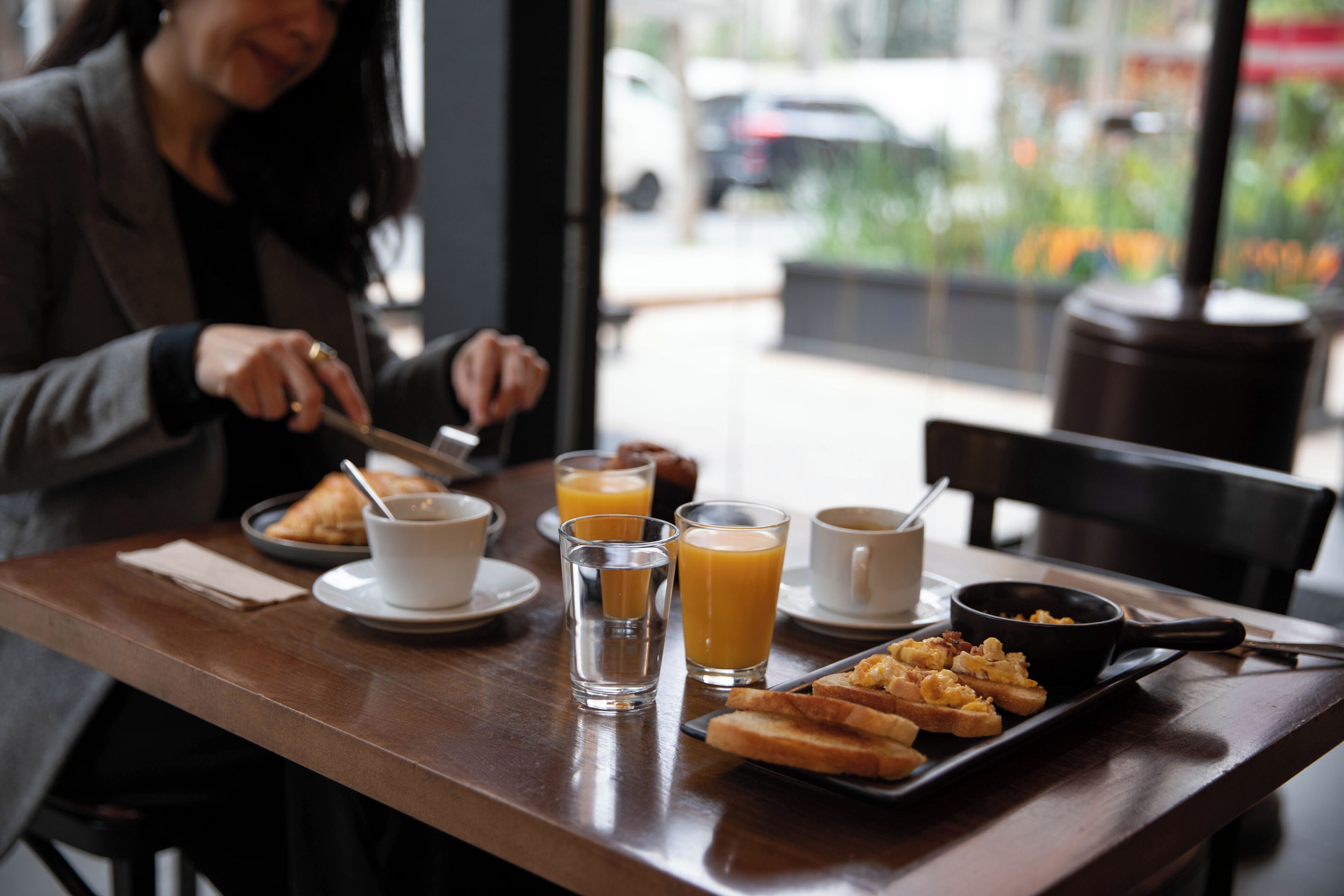 A dining table with breakfast items including toast, a pan of scrambled eggs, and glasses of orange juice.
