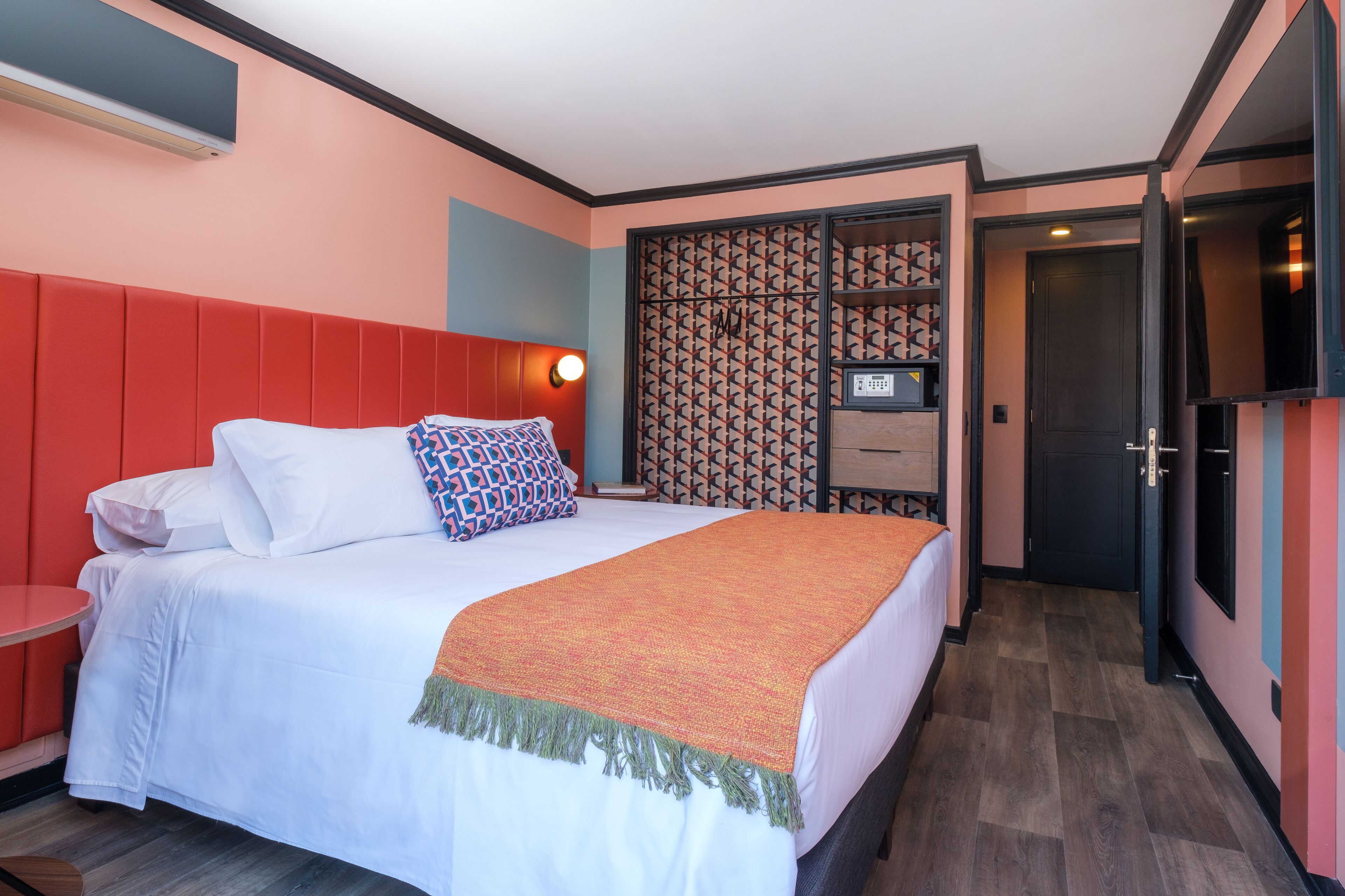 Een hotelkamer met een groot bed, een nachtkastje, een televisie en een wandpaneel met een patroon.