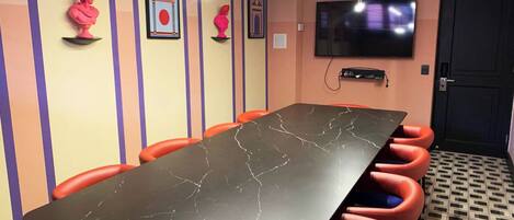 A conference room with a long table, red chairs, and a TV on the wall.