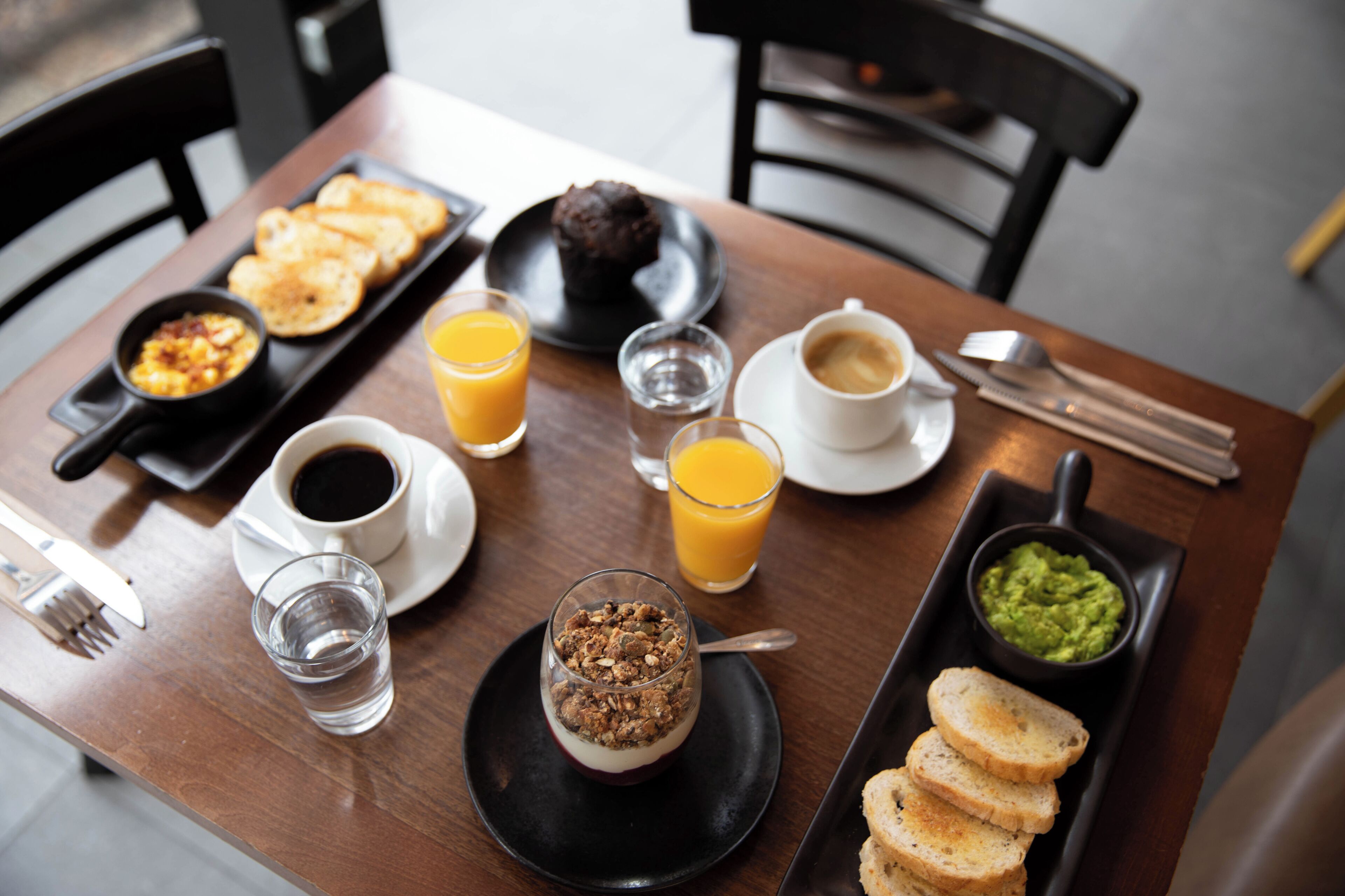 A breakfast table with toast, muffins, coffee, juice, and a bowl of guacamole.