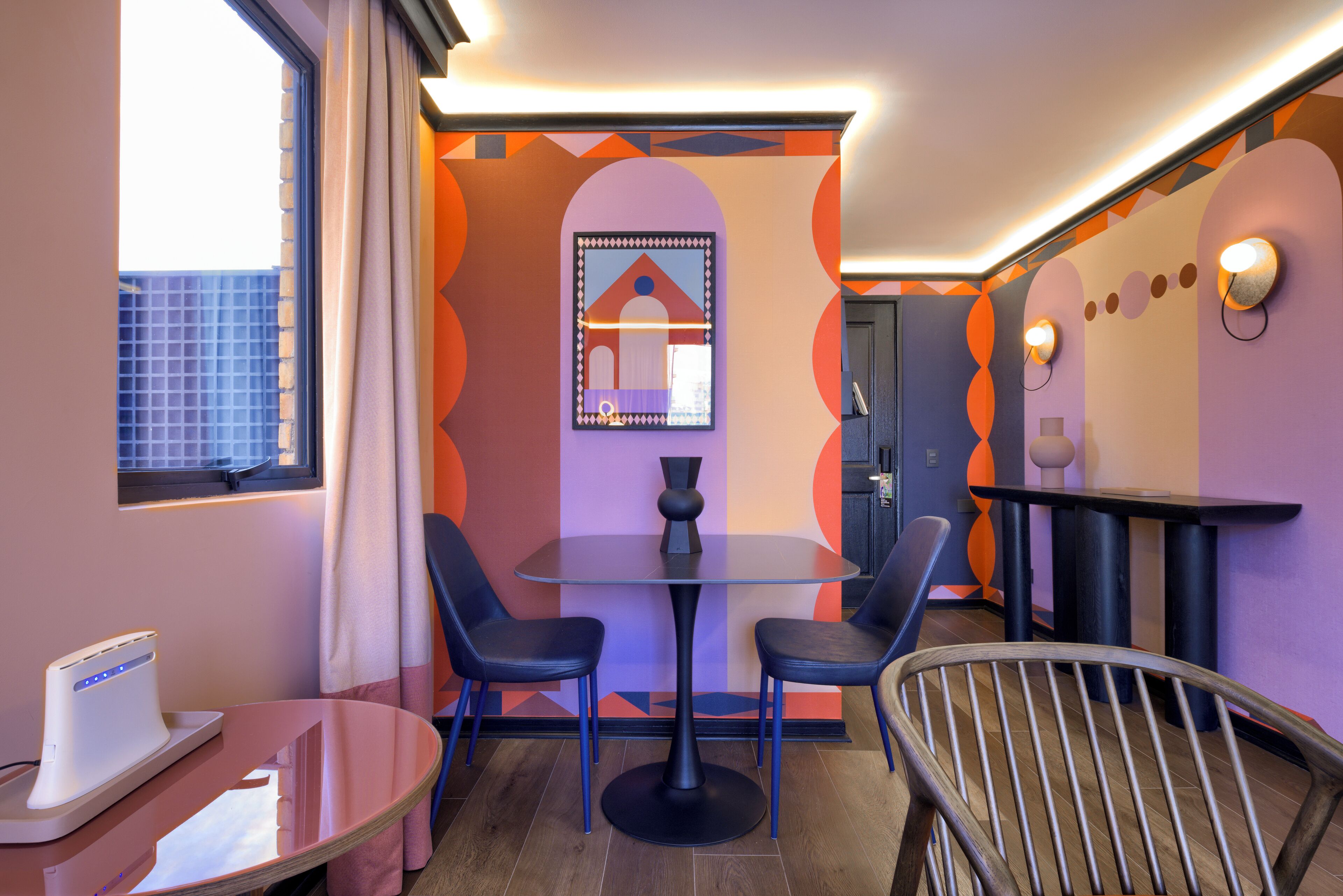 A modern room with a round table, two chairs, a small table with a device, and a window with curtains.