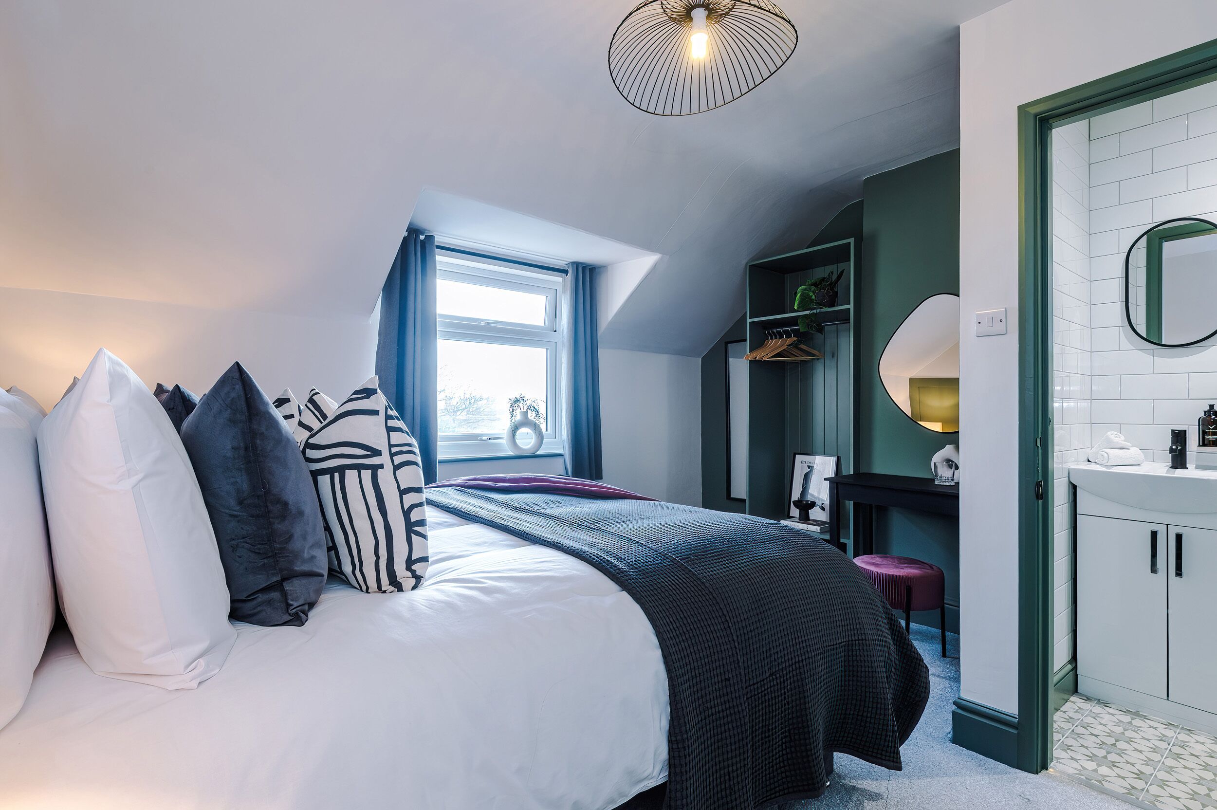 Une chambre avec un grand lit, une fenêtre avec des rideaux, une table de chevet, un miroir et une armoire.