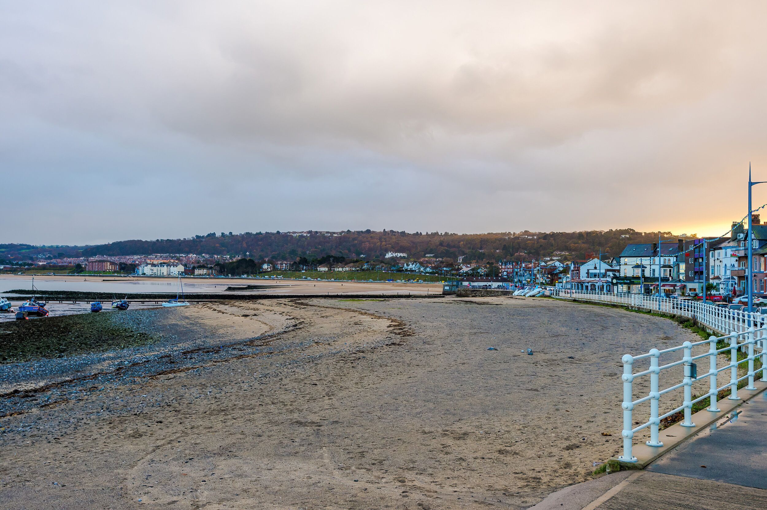A beach with a white fence, a row of houses, and a distant hill.