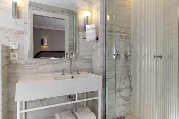 Un baño moderno con un lavamanos blanco, un espejo, una cabina de ducha de vidrio y paredes de mármol.
