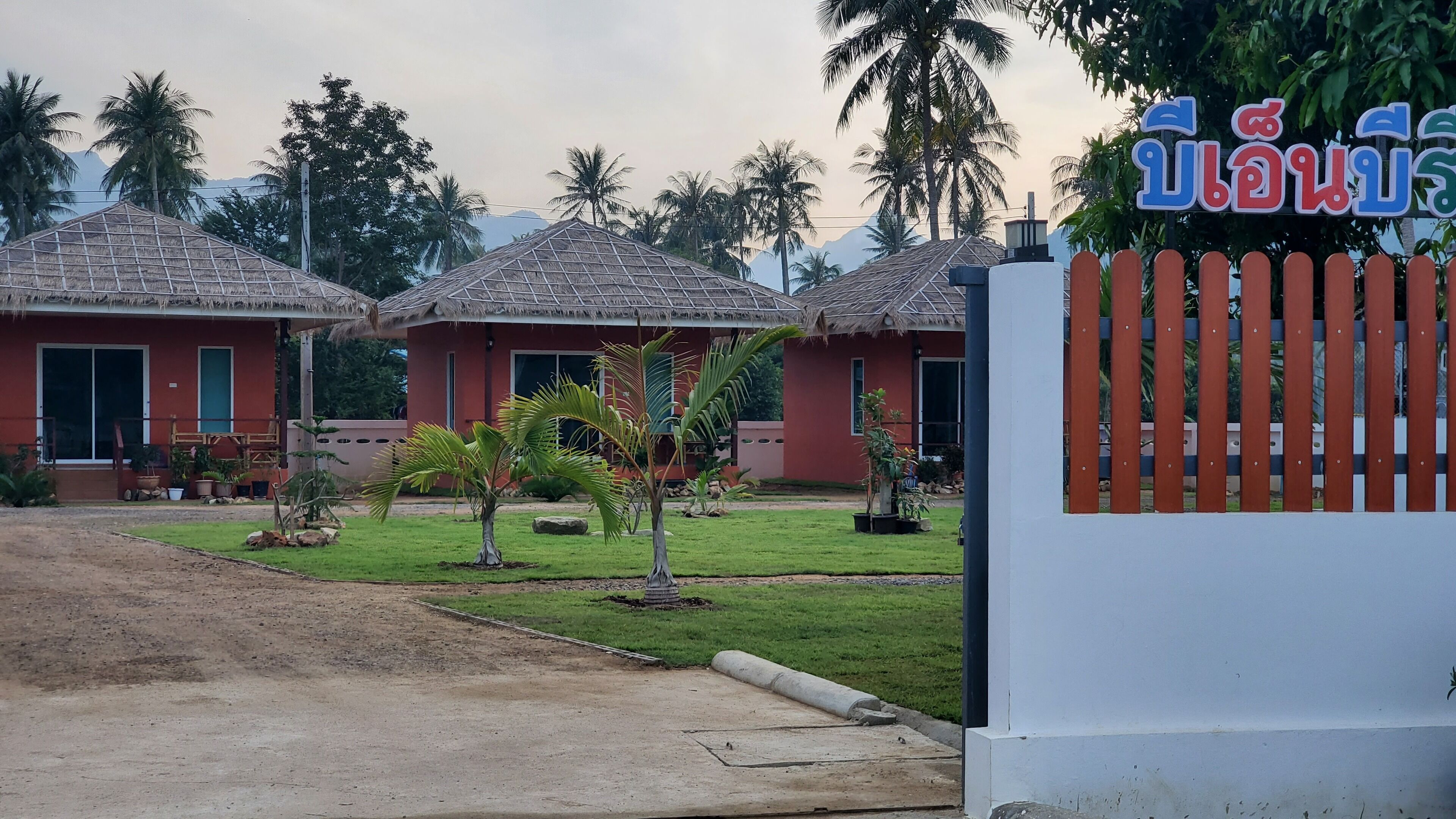 A resort with thatched-roof buildings, a well-maintained lawn, and a signboard with text.
