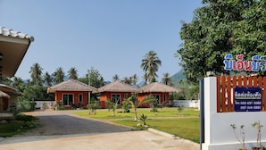 A resort with two thatched-roof cottages, a paved driveway, and a signboard with contact information.