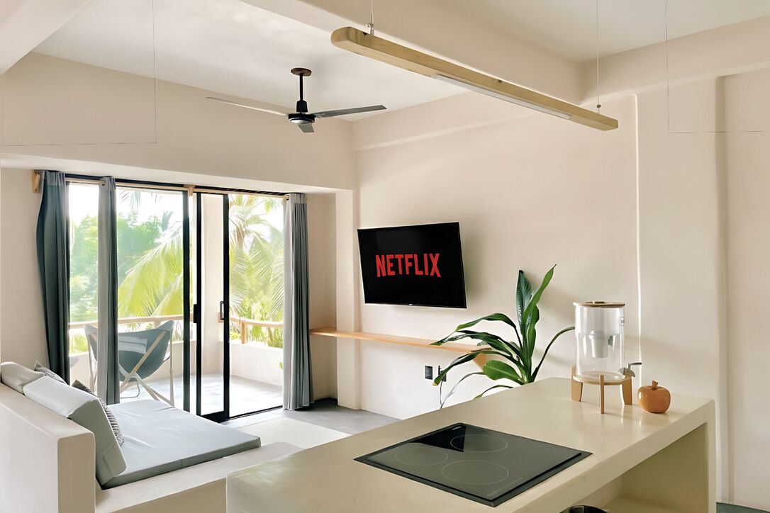 Una sala de estar moderna con una televisión de pantalla plana, un ventilador de techo y un balcón con vistas a palmeras.