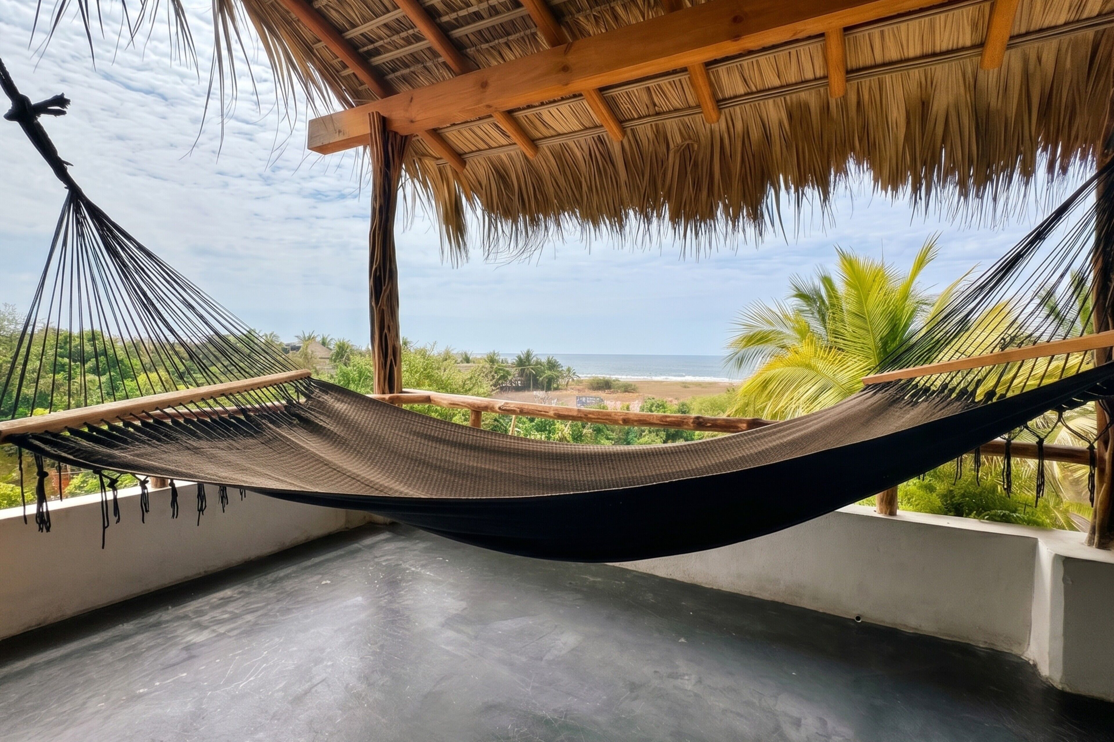 Una hamaca bajo techo de paja, vista al mar y palmeras.