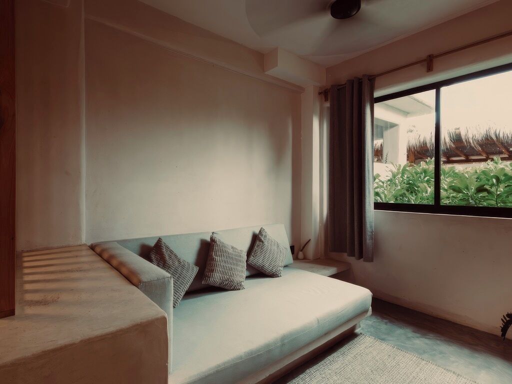 A modern living room with a sofa, a large window, and a view of greenery outside.