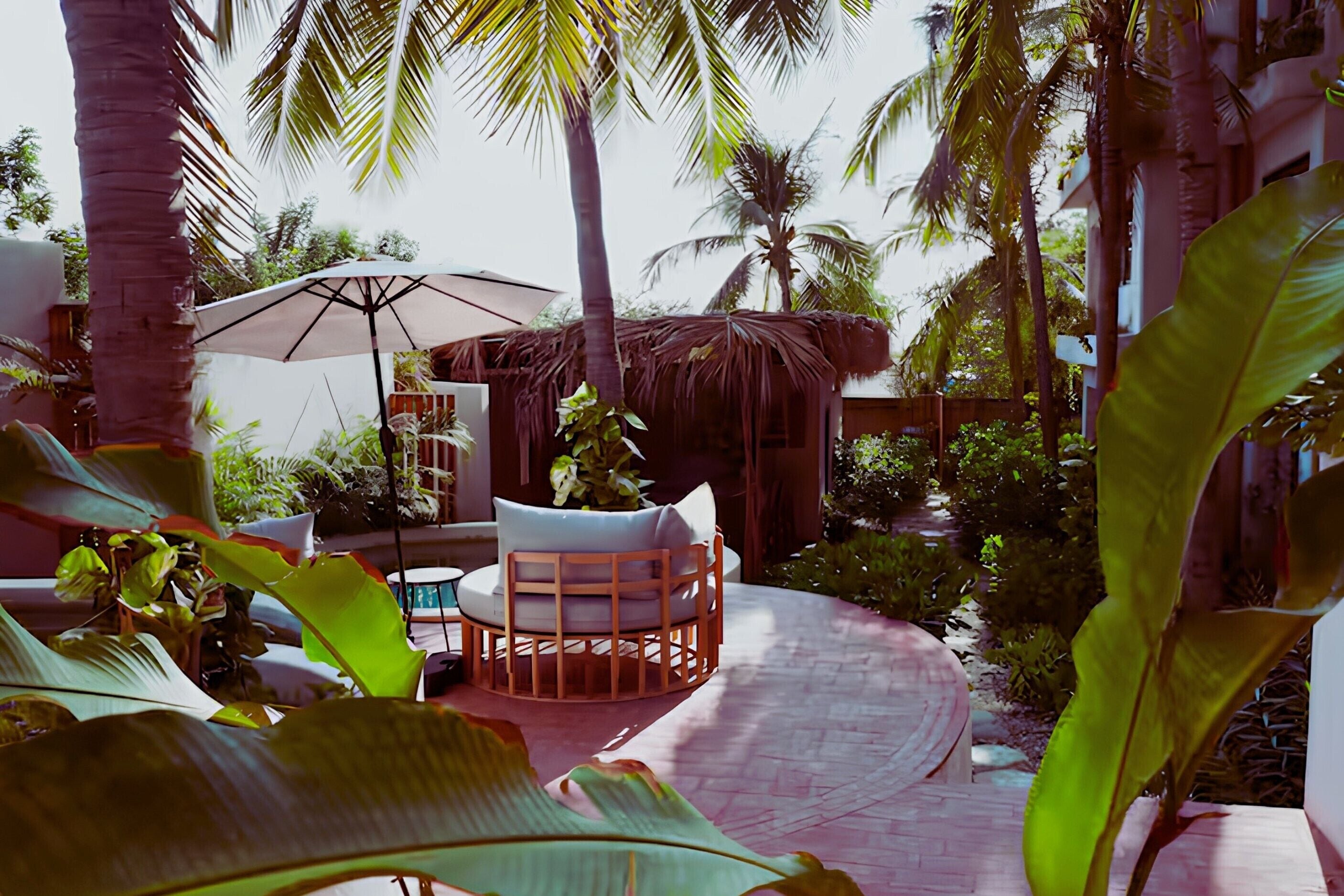 A tropical outdoor seating area with a thatched roof, a cushioned chair, and a large umbrella.