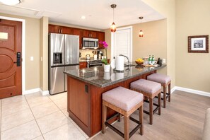 A modern kitchen with a central island, stainless steel appliances, and a seating area with cushioned stools.
