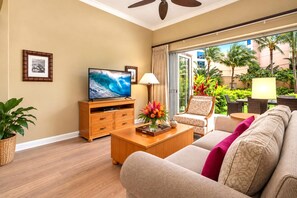 A hotel room with a television, wooden furniture, a sofa, a coffee table, and a view of the outdoors.