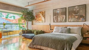 Un dormitorio moderno con una cama grande, cabecera de madera, un escritorio y vistas a un paisaje urbano a través de un ventanal.