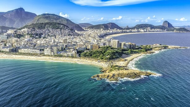 Vista aérea de una ciudad costera con una montaña destacada, una playa y una zona urbana densamente construida.