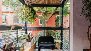 Un balcón con una silla negra, un banco de madera y plantas en macetas.