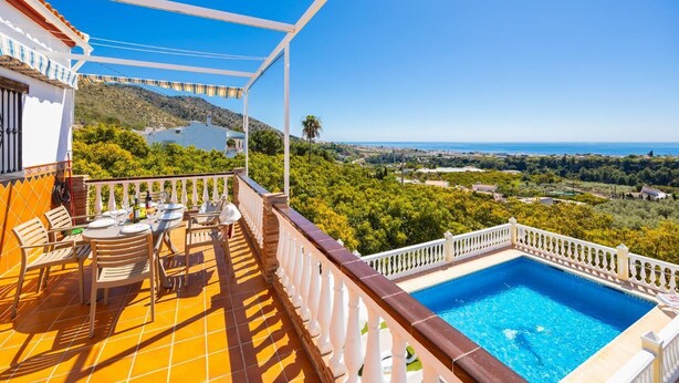 A balcony with a pool, outdoor furniture, and a view of the sea and hills.