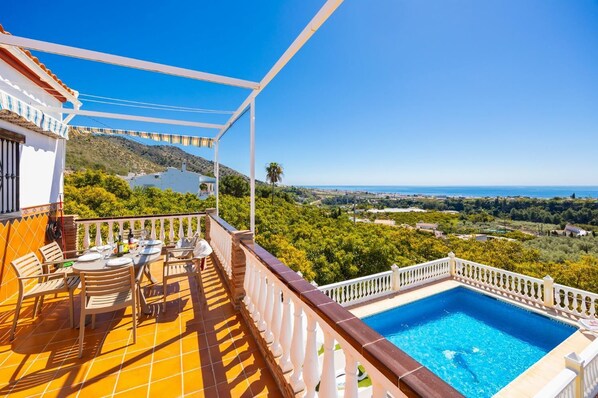 Ein Balkon mit Pool, Gartenmöbeln und Blick auf Meer und Hügel.