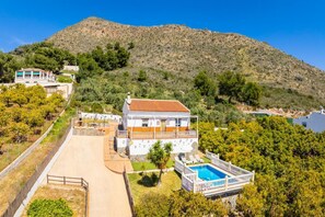 Ein zweistöckiges Haus mit Swimmingpool, umgeben von viel Grün und einer Hügelkulisse im Hintergrund.