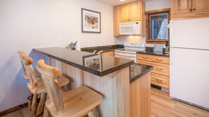 Une cuisine avec des meubles en bois, un four à micro-ondes, une cuisinière et un réfrigérateur. Il y a également un coin bar avec des tabourets.