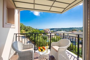Een balkon met rieten meubilair, een tafel met fruit en uitzicht op een stad en heuvels.