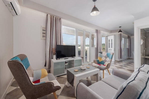 A modern living room with a flat-screen TV, two armchairs, a sofa, and a dining table.