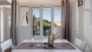 Un coin repas avec une table dressée pour deux personnes, un vase contenant des plantes séchées et une vue sur la verdure à l’extérieur.
