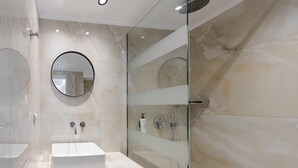 Une salle de bain moderne avec un meuble-lavabo en marbre, un miroir rond et une douche séparée par des parois en verre.