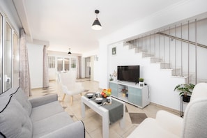 A modern living room with a sofa, a coffee table, and a TV. There is a staircase with a railing and a plant on the side.