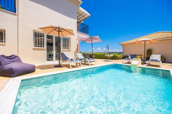A poolside area with lounge chairs, umbrellas, and a building with balconies.