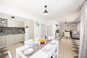 A modern kitchen with a dining area, a sofa, and a staircase leading to another level.