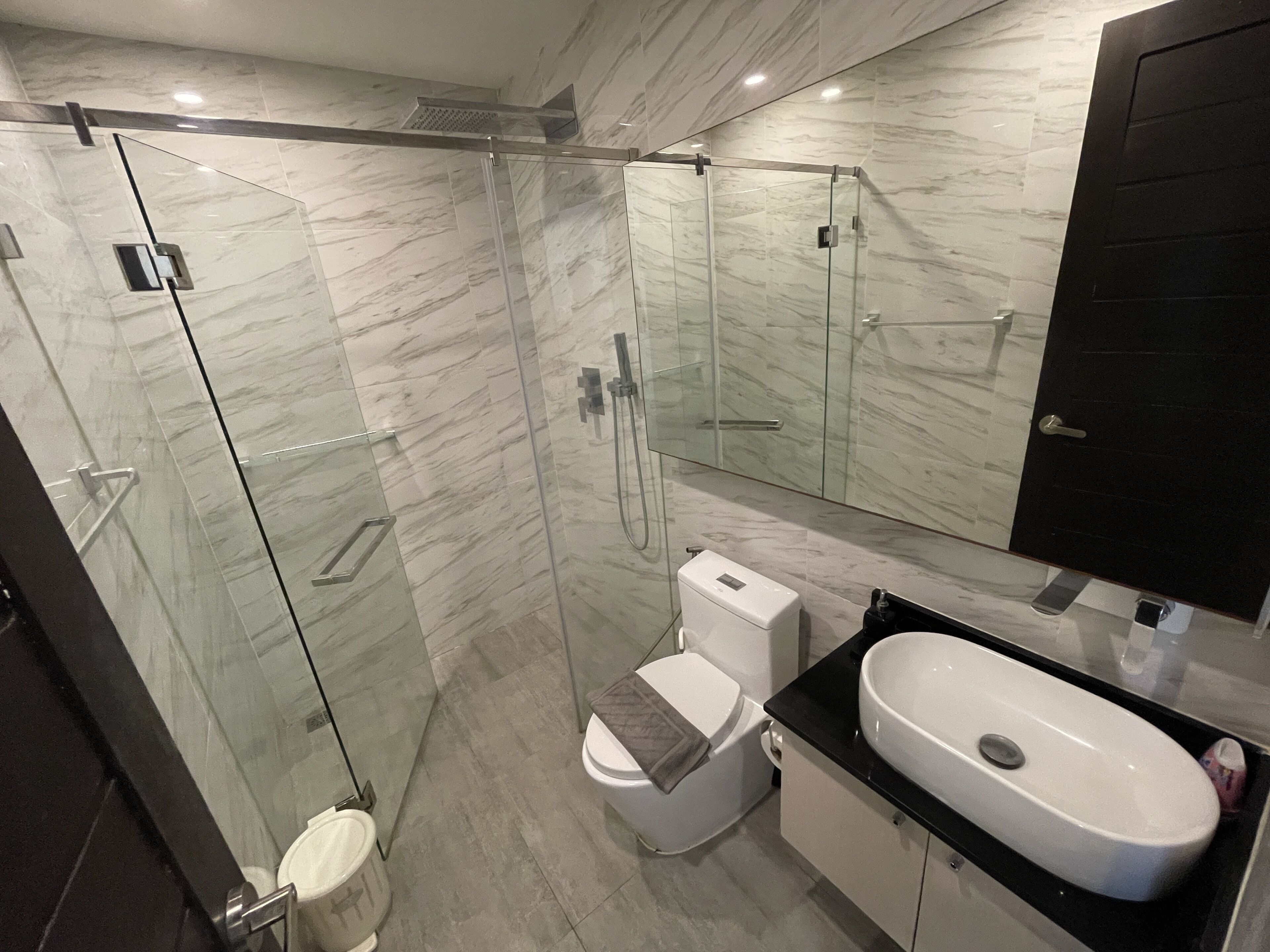 A modern bathroom with a glass-enclosed shower, a toilet, and a sink with a black countertop.