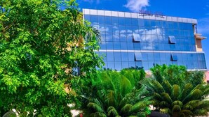 A modern hotel building with a glass facade, surrounded by lush greenery and palm trees. - Muhako Hotel (Dar es Salaam)
