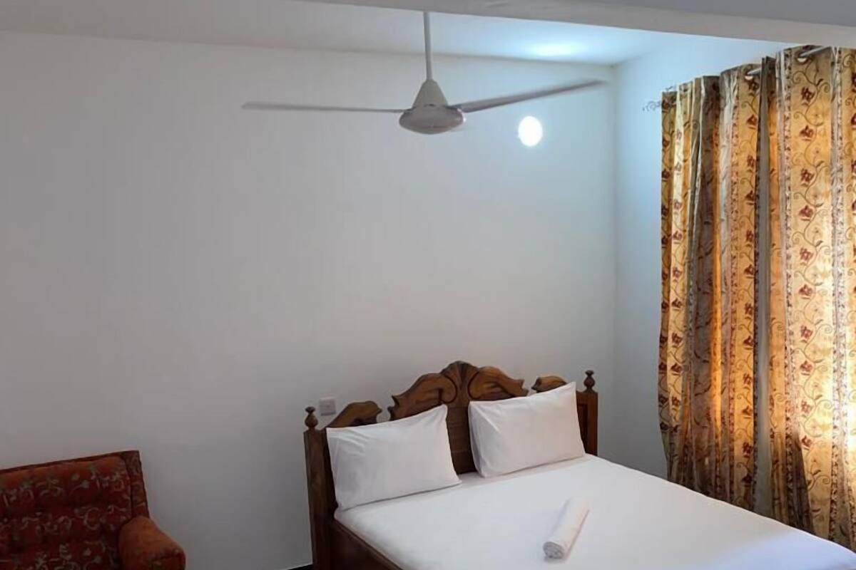 Un dormitorio con una cama de madera, un ventilador de techo, un sillón rojo estampado y una cortina con motivos.