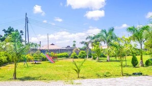 A playground with a slide and swings, surrounded by grass and palm trees. - Muhako Hotel (Dar es Salaam)