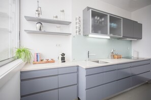 A modern kitchen with grey cabinets, a white countertop, and a window with a plant. - Liiiving - Light Trendy Apartment (Porto)