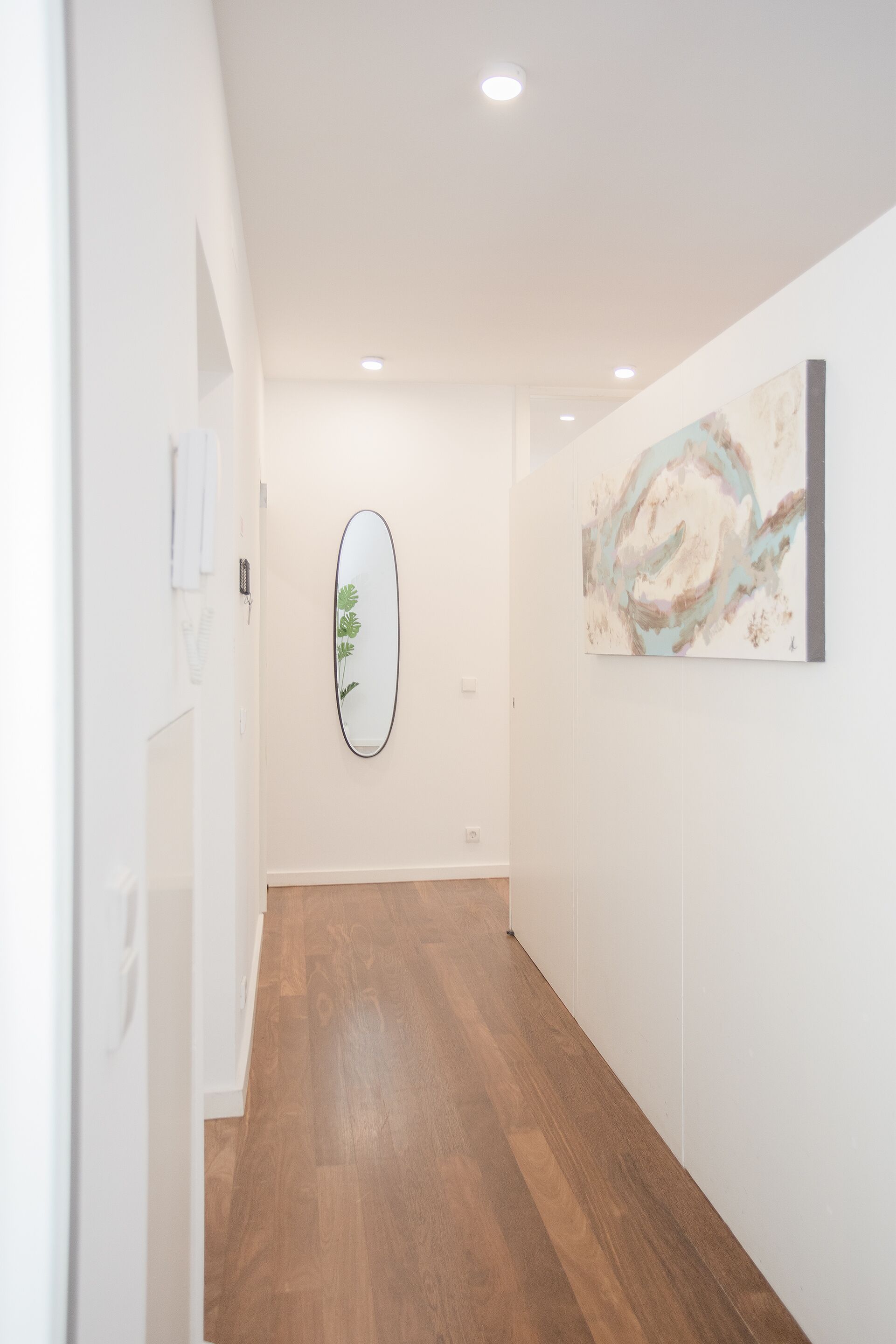 A hallway with wooden flooring, white walls, and a ceiling with recessed lighting.