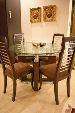 A dining area with a glass-top table surrounded by four wooden chairs with cushioned seats. Two framed artworks are hung on the wall above the table. - Peaceful Couple's Gateway APT (Rawalpindi)