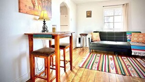 Una sala de estar con una mesa de comedor de madera, un sofá y una alfombra colorida.