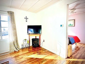 A room with a fireplace, a television mounted above it, and a bed with a red blanket. - La Casita | Southwest Studio Near Downtown Raton (Raton)